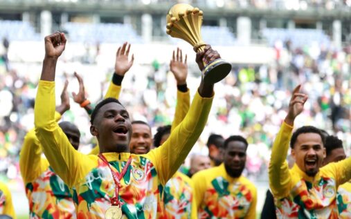 Senegal football players lifting and celebrating with the Africa Cup of Nations trophy in front of fans at Stade de France.