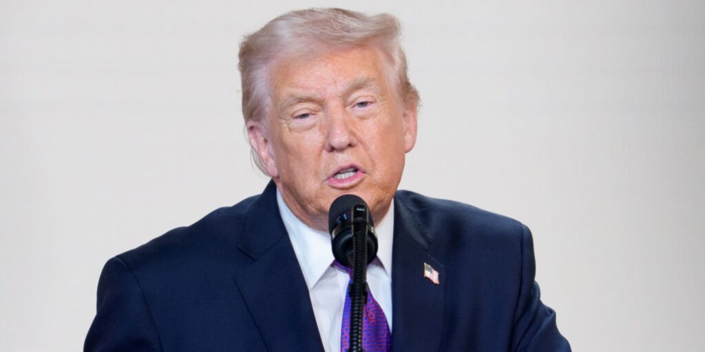 Donald Trump speaking at a podium with the United States flag in the background