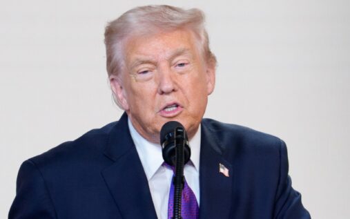 Donald Trump speaking at a podium with the United States flag in the background