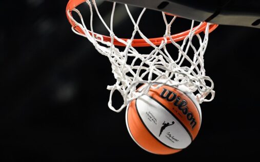 WNBA commissioner Cathy Engelbert speaking at a press conference alongside an official league logo