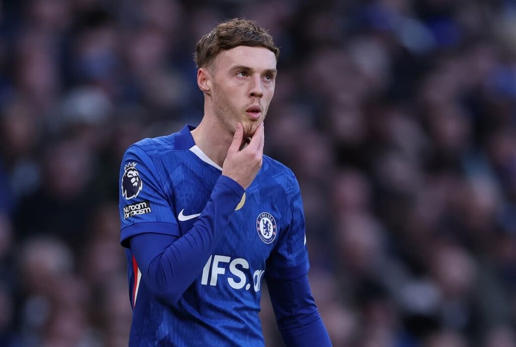 Cole Palmer looking thoughtful on the pitch in a Chelsea football kit