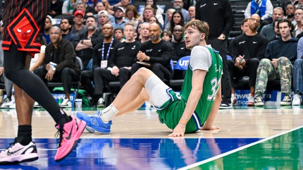 Dallas Mavericks forward Cooper Flagg sitting on the basketball court grasping his injured left ankle