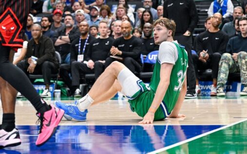 Dallas Mavericks forward Cooper Flagg sitting on the basketball court grasping his injured left ankle