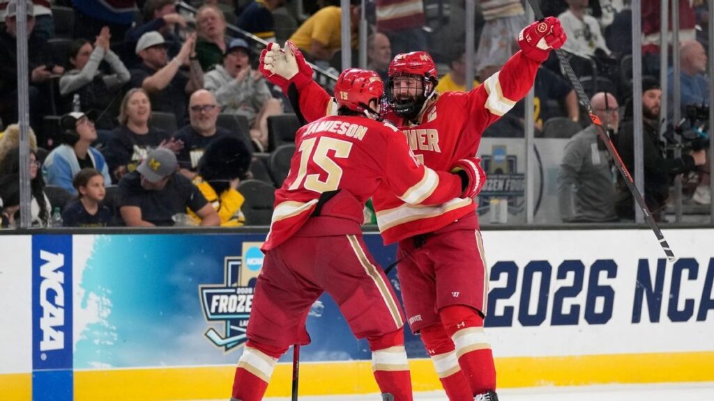 Denver Pioneers players celebrating their double-overtime victory on the ice against the Michigan Wolverines