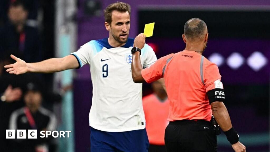 A football referee holding up a yellow card during a competitive international match
