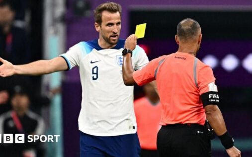 A football referee holding up a yellow card during a competitive international match