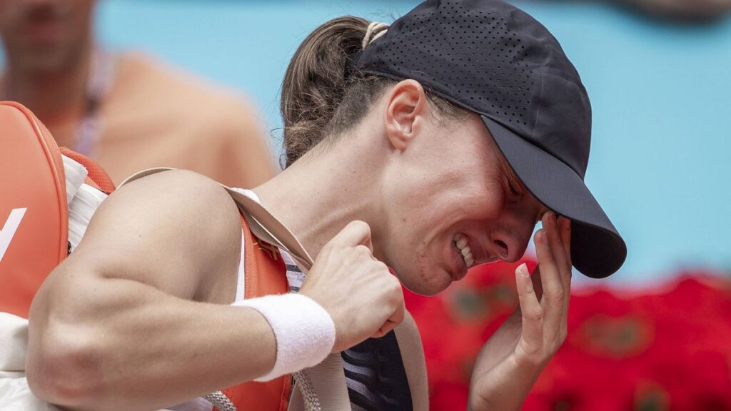 Iga Swiatek appearing visibly distressed and receiving medical attention on a clay tennis court