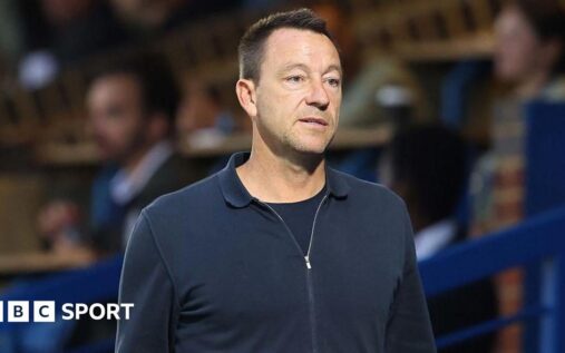 John Terry wearing a suit standing on the touchline during a football match