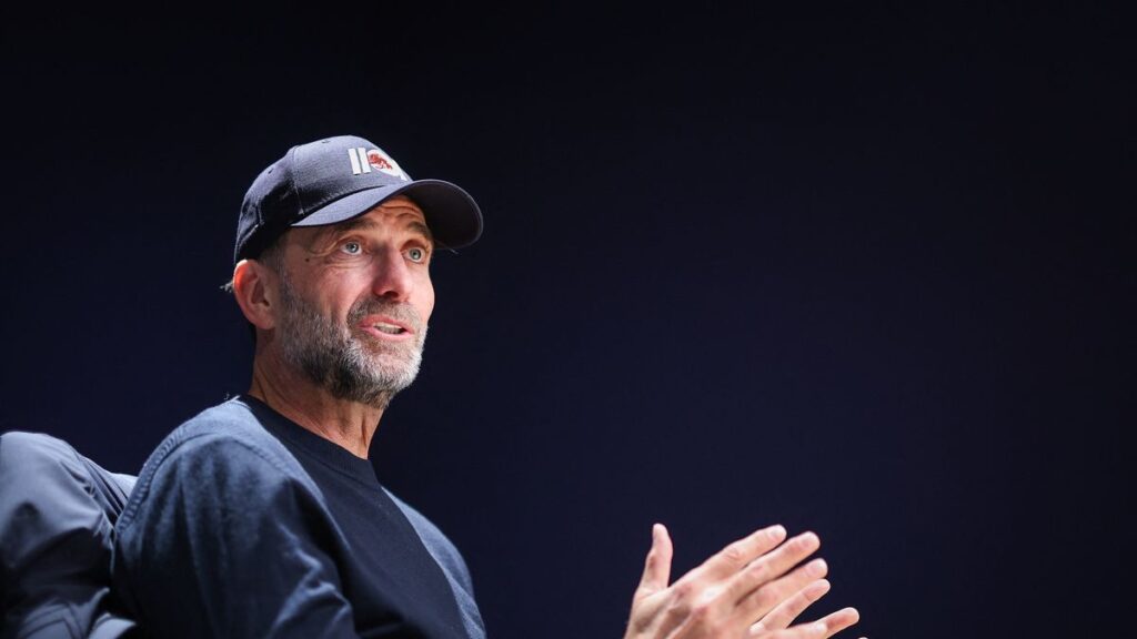 Jurgen Klopp smiling while watching a football match from the stands