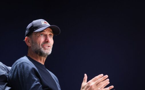 Jurgen Klopp smiling while watching a football match from the stands