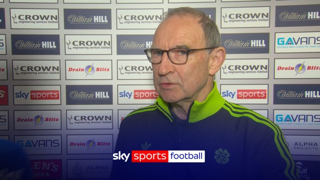 Martin O'Neill smiling while watching a football match from the stands
