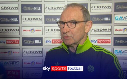 Martin O'Neill smiling while watching a football match from the stands