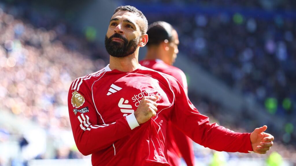 Mohamed Salah wearing a red Liverpool kit looking thoughtful on the football pitch