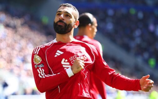 Mohamed Salah wearing a red Liverpool kit looking thoughtful on the football pitch