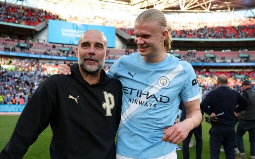 Pep Guardiola smiling on the Manchester City touchline wearing a casual sweatshirt