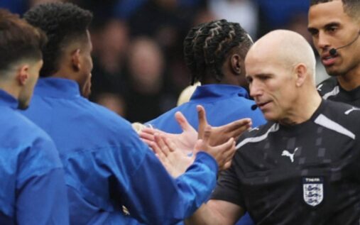 Assistant referee Richard West holding a flag on the touchline during a Premier League football match