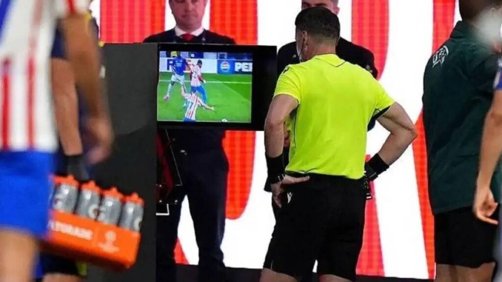 Referee looking at a pitchside VAR monitor during a Champions League match