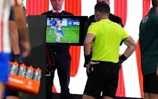 Referee looking at a pitchside VAR monitor during a Champions League match