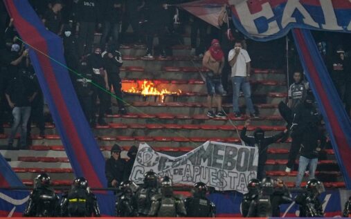 Referee ordering football players off the pitch amid flares and smoke at a South American stadium