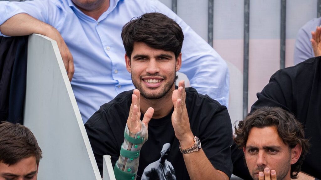Carlos Alcaraz looking disappointed on a tennis court with a strapped wrist