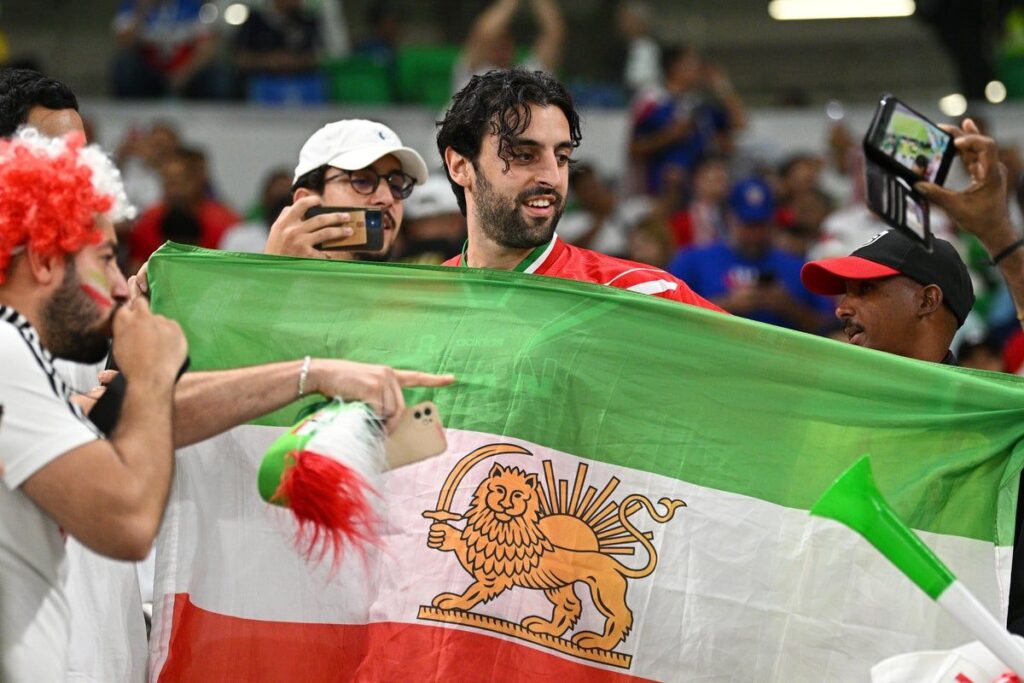 Fans holding the pre-revolutionary Iran flag featuring the traditional lion and sun emblem