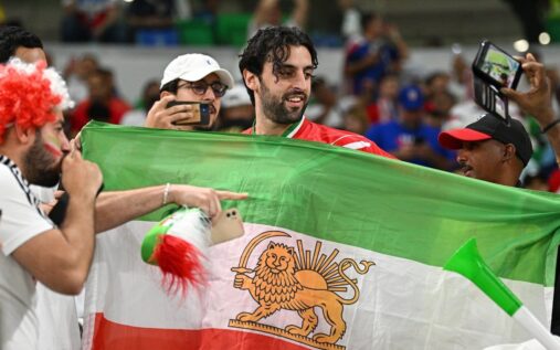 Fans holding the pre-revolutionary Iran flag featuring the traditional lion and sun emblem