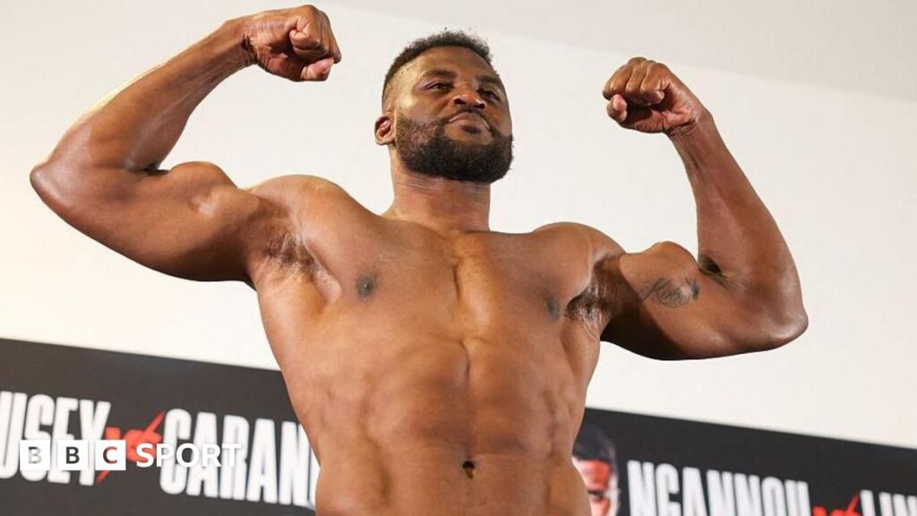 Francis Ngannou posing with his mixed martial arts championship belt inside the fighting cage