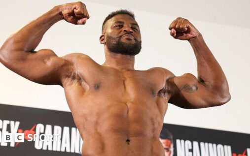 Francis Ngannou posing with his mixed martial arts championship belt inside the fighting cage