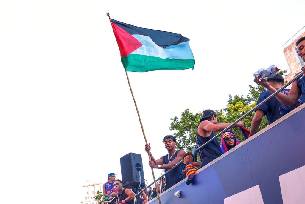 Barcelona winger Lamine Yamal waving a Palestinian flag from an open-top bus