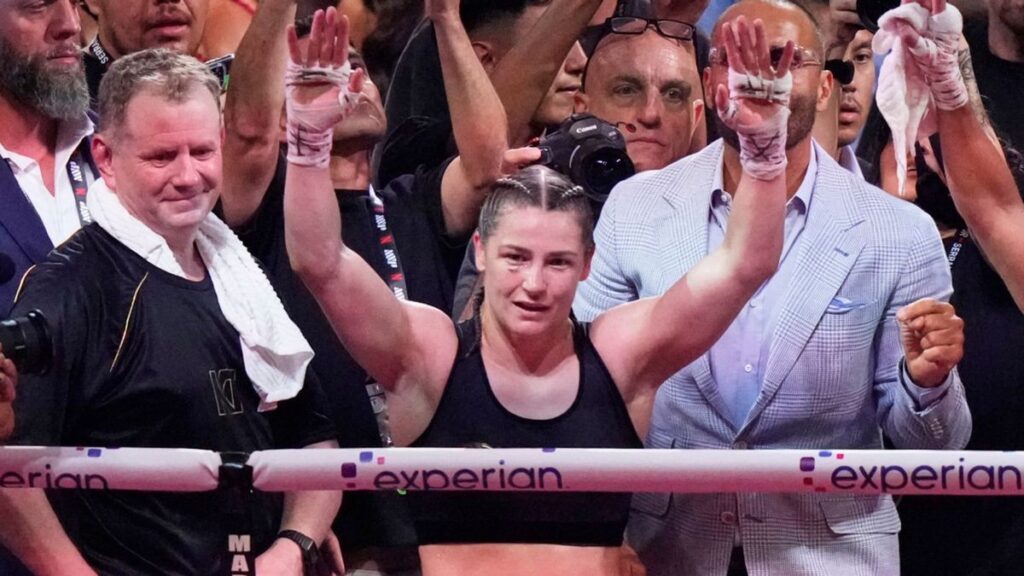Katie Taylor holding her championship boxing belts after a victory in the ring