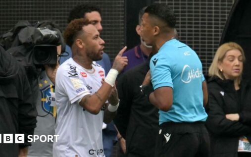 Neymar looking furious on the touchline while holding up a substitution slip to a camera
