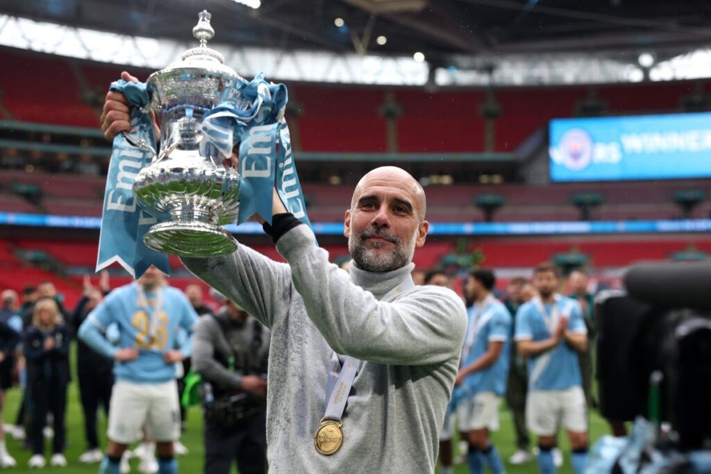 Manchester City manager Pep Guardiola celebrating on the pitch with his squad after winning the FA Cup trophy.