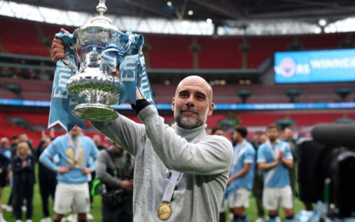 Manchester City manager Pep Guardiola celebrating on the pitch with his squad after winning the FA Cup trophy.