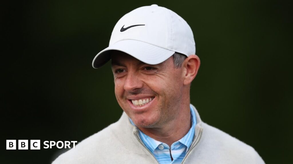Rory McIlroy smiling and waving to the crowd while walking on a golf course