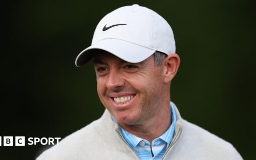 Rory McIlroy smiling and waving to the crowd while walking on a golf course