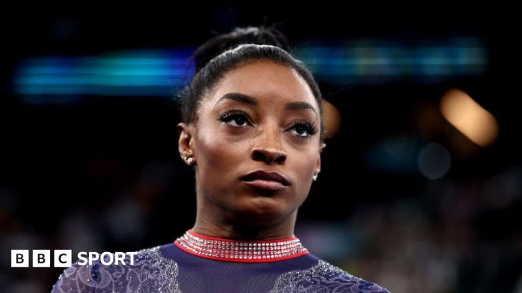 Simone Biles smiling and waving to the crowd while competing in gymnastics