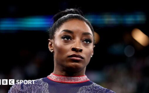 Simone Biles smiling and waving to the crowd while competing in gymnastics