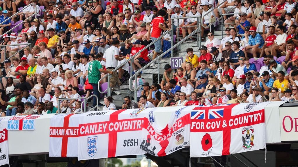 England football fans waving flags and cheering in the stands during an international match