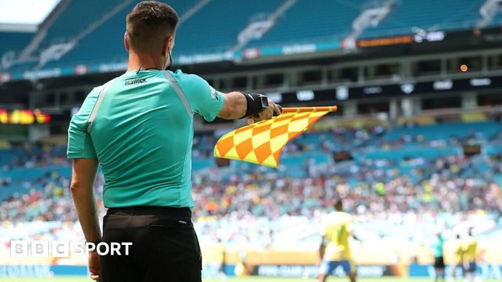 A referee's assistant raising an offside flag on the touchline during a football match