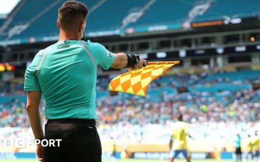 A referee's assistant raising an offside flag on the touchline during a football match