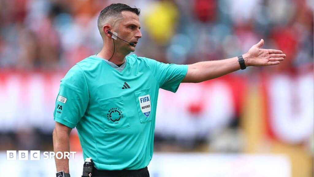 Referee pointing to their watch during a football match to indicate timekeeping rules