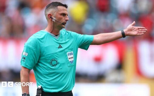 Referee pointing to their watch during a football match to indicate timekeeping rules