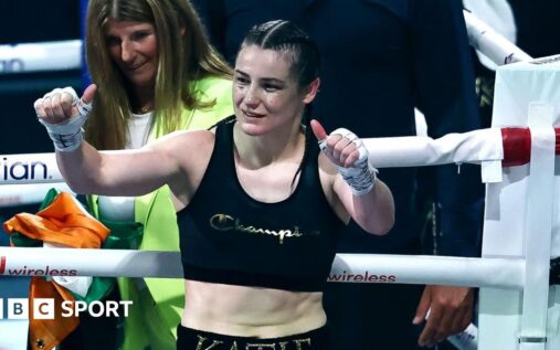 Katie Taylor wearing boxing gloves and holding her undisputed world championship belts