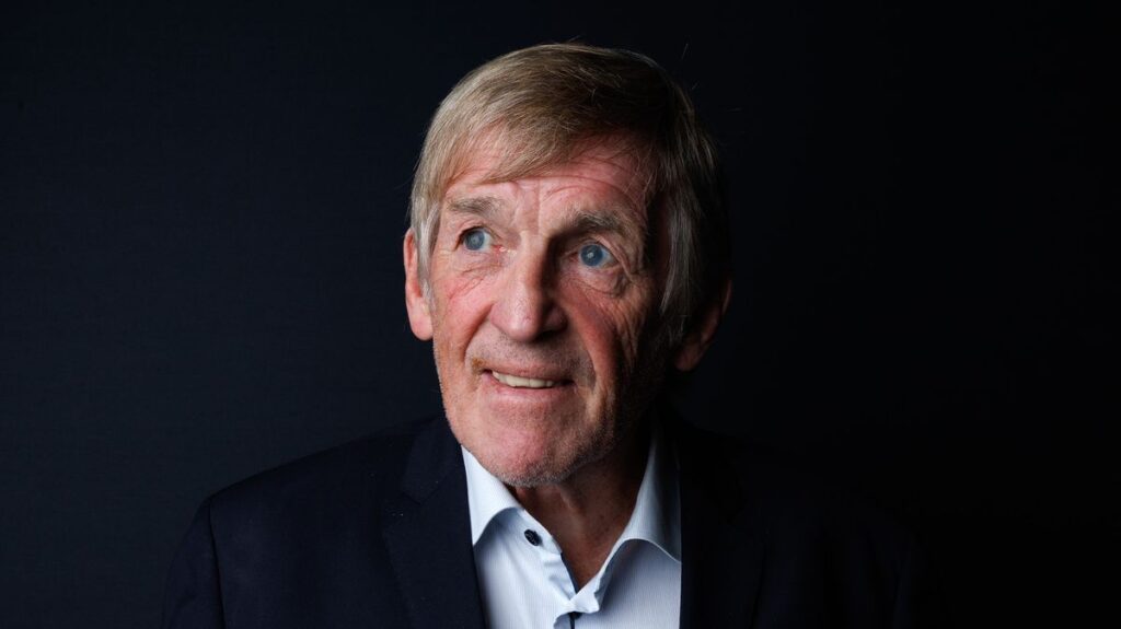 Sir Kenny Dalglish smiling at Anfield while wearing a Liverpool FC scarf