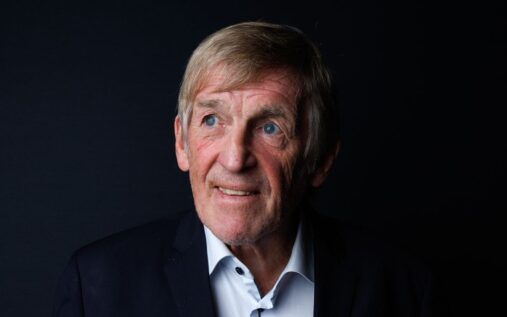 Sir Kenny Dalglish smiling at Anfield while wearing a Liverpool FC scarf