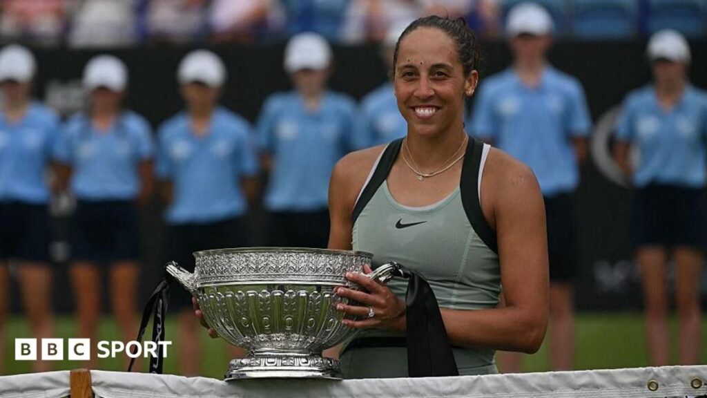 Madison Keys smiling while holding the Eastbourne International winner's trophy on a grass court