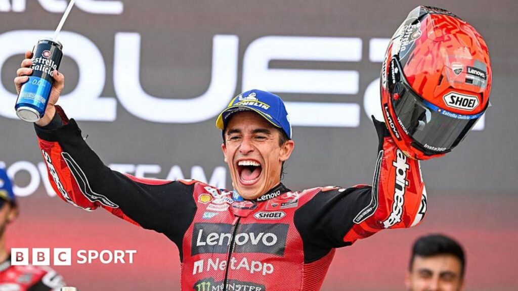 Marc Marquez standing on his Ducati motorcycle to celebrate his 100th career victory with a red flag