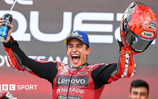 Marc Marquez standing on his Ducati motorcycle to celebrate his 100th career victory with a red flag