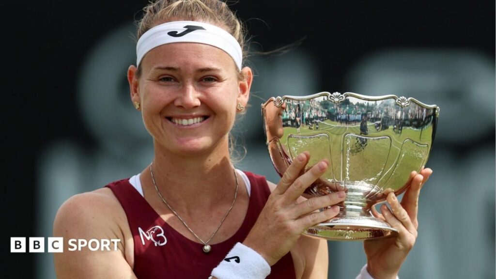 Marie Bouzkova holding the Nottingham Open trophy and smiling on a grass court
