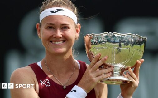 Marie Bouzkova holding the Nottingham Open trophy and smiling on a grass court